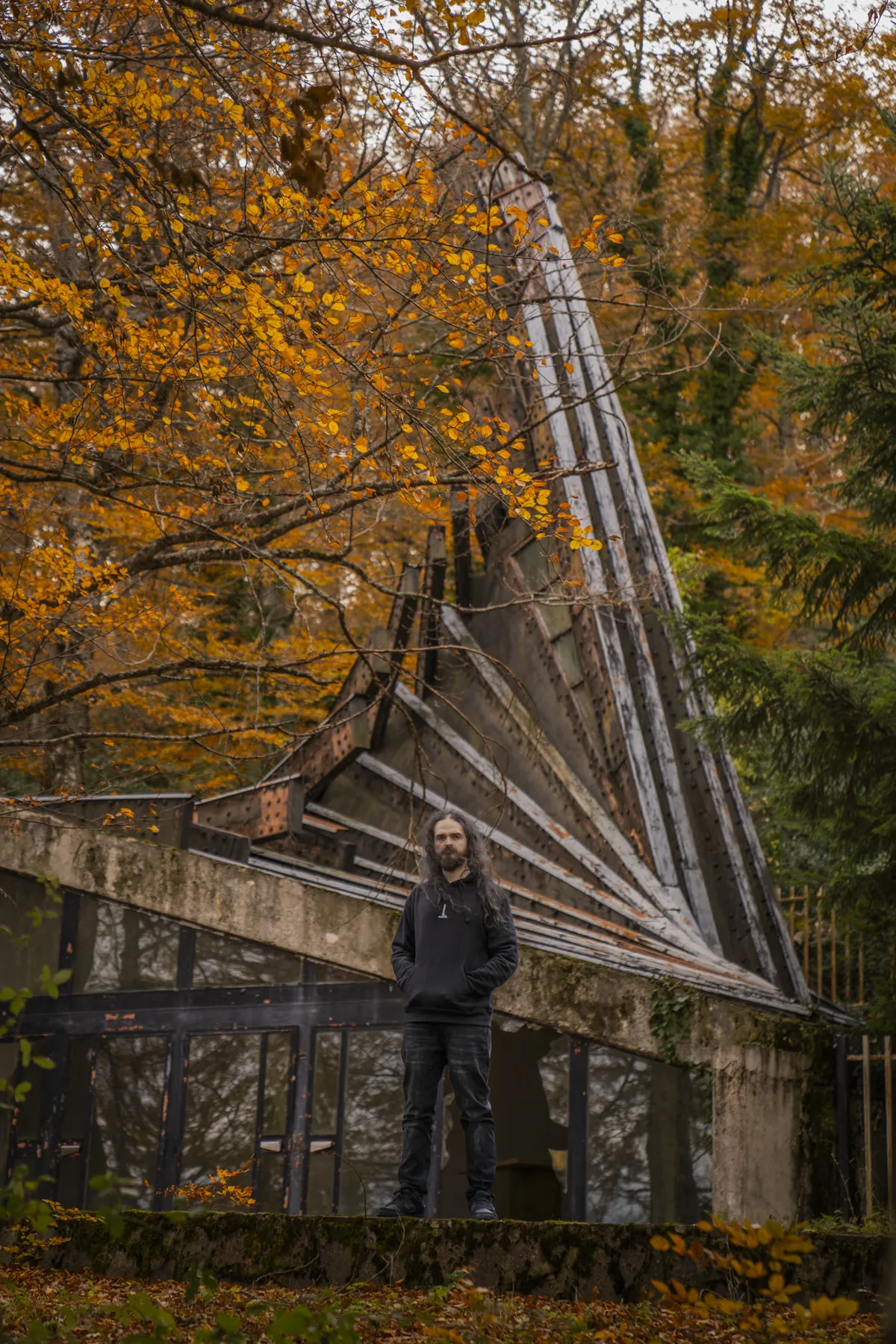 The luthier standing in front of a brutalist concrete structure among autumn trees